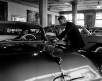 Poster print of two mid-adult men admiring a car in an automobile showroom.