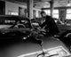 Poster print of two mid-adult men admiring a car in an automobile showroom.