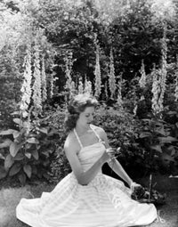 Young woman sitting in garden holding flower poster print.