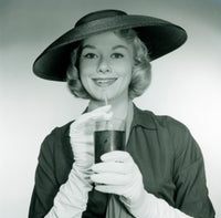 Studio portrait of a smiling young woman wearing a hat and gloves, holding a glass.