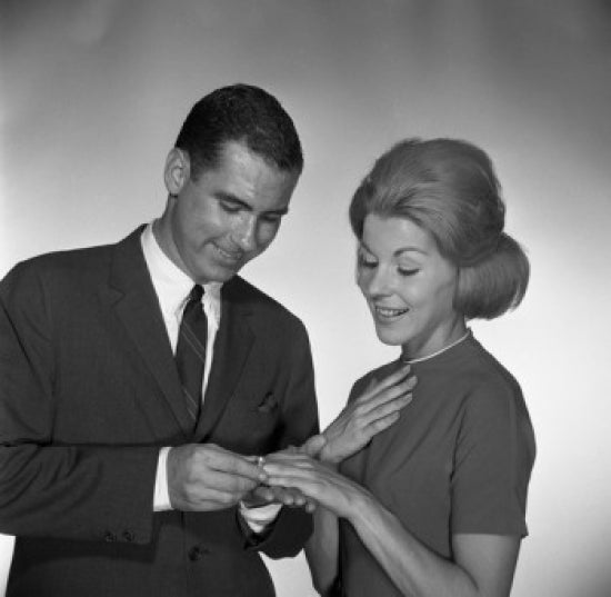 Engagement moment poster print showing a man placing a ring on a woman's palm in a studio shot.