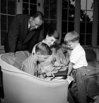 Family with three boys viewing photograph album in living room poster print
