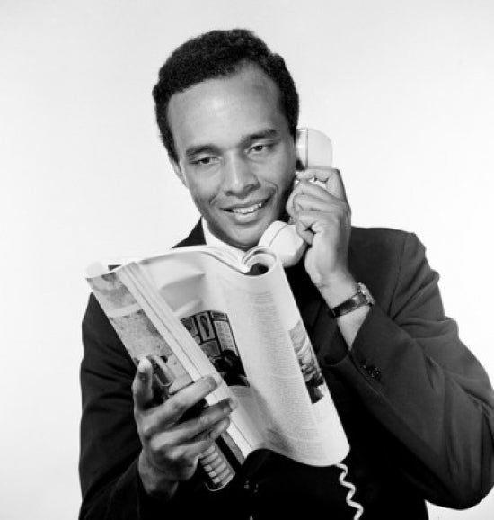 Portrait of African American man holding receiver and reading magazine in a studio shot.