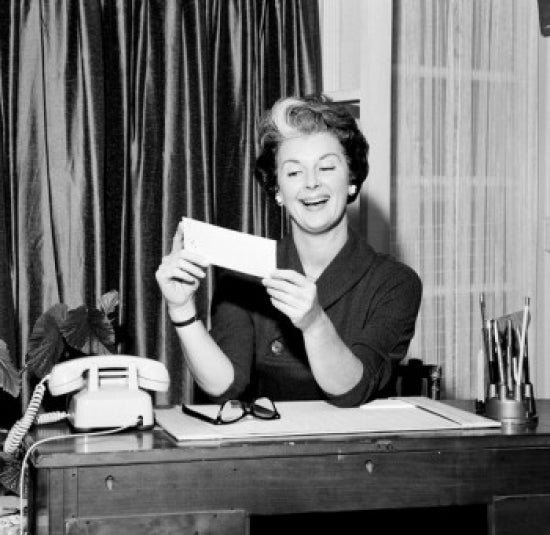 Mid adult woman sitting at desk holding paycheck poster print.