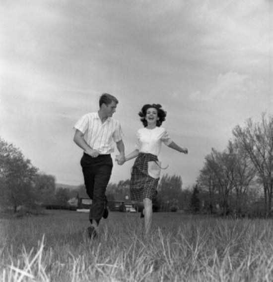 Young couple running through a green field poster print.