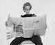 Mid adult woman reading a financial newspaper with a thoughtful expression.