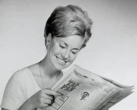 Close-up of a young woman reading a newspaper poster print.