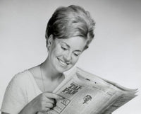 Close-up of a young woman reading a newspaper poster print.