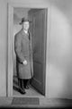Mid adult man wearing overcoat and hat emerging from door poster print