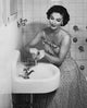 Poster print of a young woman washing her hands in the bathroom sink.