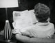 Poster print featuring the rear view of a young woman reading a newspaper.