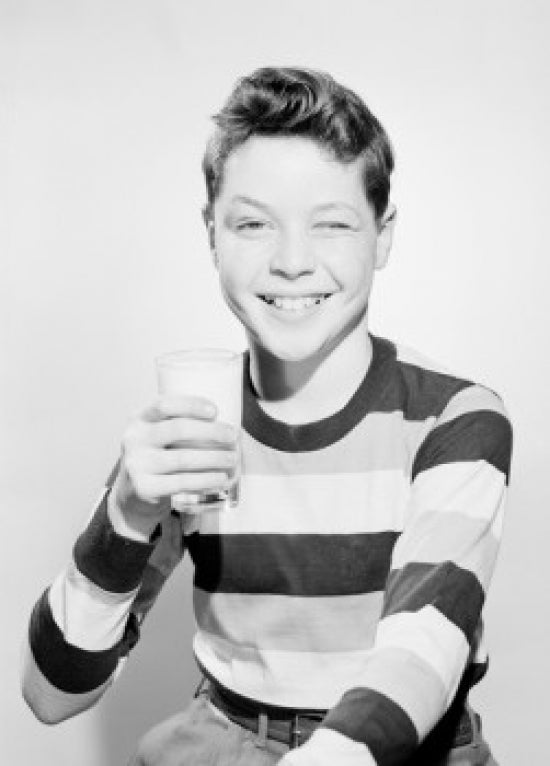 Studio portrait of a boy holding a glass of milk, joyful childhood moment.