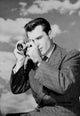 Young man using camera against a cloudy sky poster print