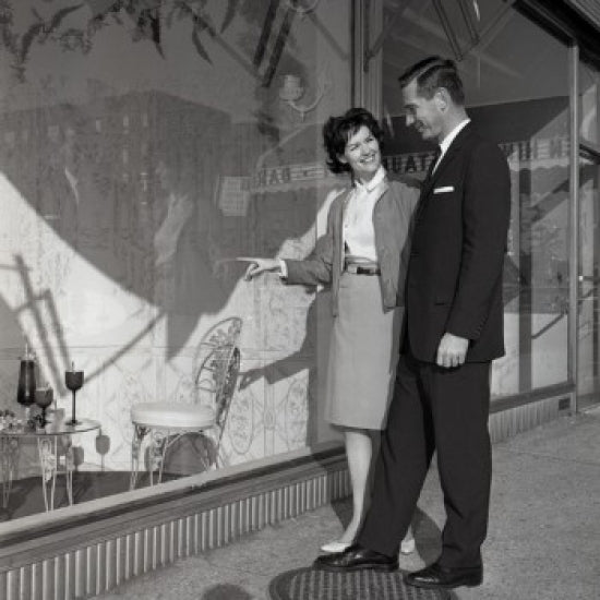 Mid adult couple admiring a window display poster print.