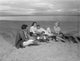 Group of young friends resting by a bonfire on a sandy beach poster print.