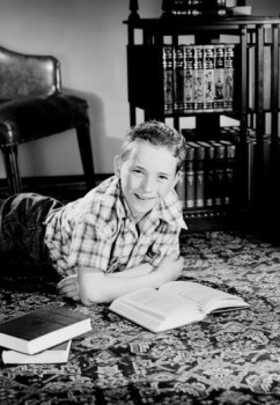 Poster print of a boy lying on the floor in a living room reading books.