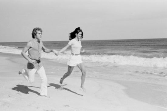 Young couple joyfully running across the beach poster print