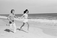 Young couple joyfully running across the beach poster print