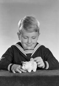 Studio shot of a boy inserting a coin into a piggy bank poster print.