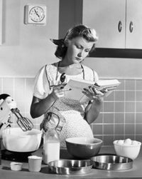 Young woman reading a cookbook in a domestic kitchen poster print.