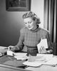 Poster print of mid adult woman sitting at a desk and sorting bills.
