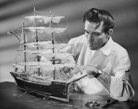 Poster of a mid adult man making a model sailing ship, showcasing craftsmanship.