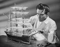 Poster of a mid adult man making a model sailing ship, showcasing craftsmanship.