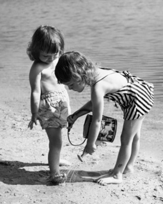 Girl pouring water on another girl's foot on the beach poster print
