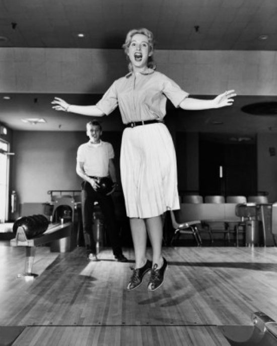 Young adult woman jumping in a bowling alley poster print.