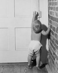 Rear view of a baby opening a door poster print