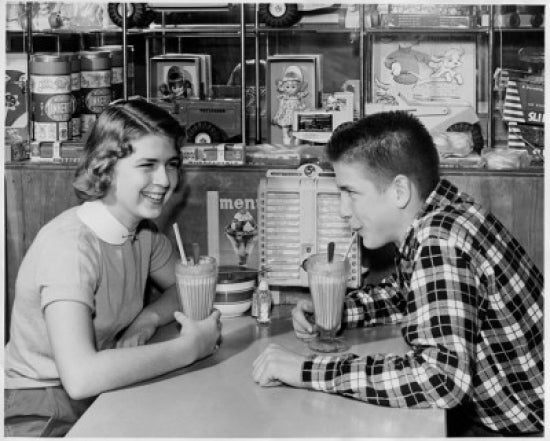 Teenage couple sharing milkshakes in a restaurant poster print.