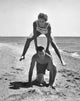 Poster print of a young couple playing leapfrog on the beach, capturing joy and playfulness.