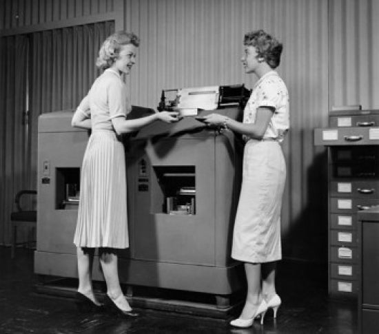 Side profile of two businesswomen standing in front of a machine poster print.