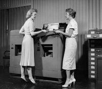 Side profile of two businesswomen standing in front of a machine poster print.