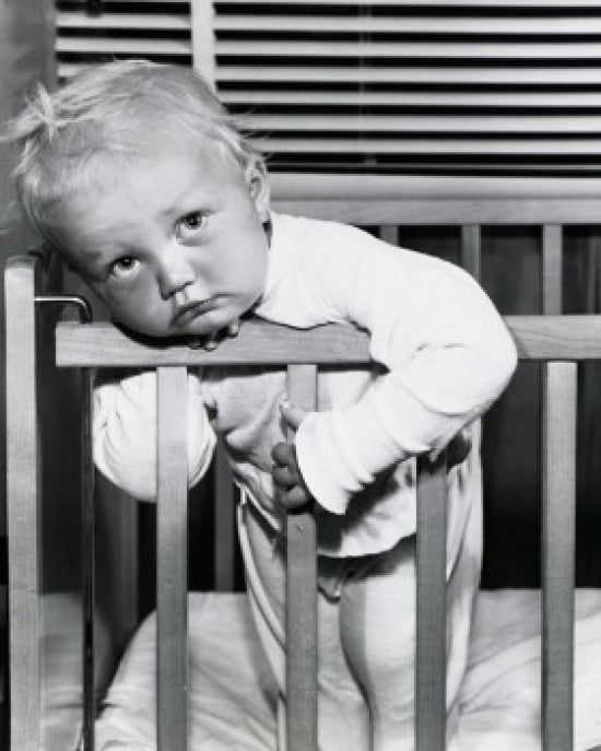Close-up of a baby boy leaning over a crib poster print.