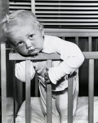 Close-up of a baby boy leaning over a crib poster print.