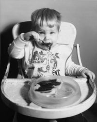 Baby sitting in high chair enjoying baby food poster print.