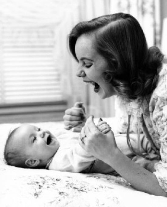 Young woman playing with baby on bed poster print