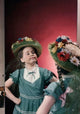 Close-up poster print of a girl wearing a floral hat looking into a mirror.
