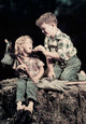 Side profile artwork of a boy feeding a girl sitting on a rock.
