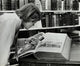 Young man examining a miniature Bible in a library setting poster print.