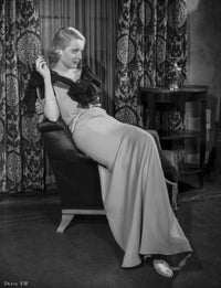 Bette Davis seated on a couch in a black ribbon top and white silk long dress photo print.