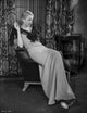 Bette Davis seated on a couch in a black ribbon top and white silk long dress photo print.