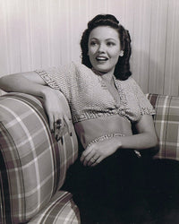 Gene Tierney sitting back on a patterned couch photo print