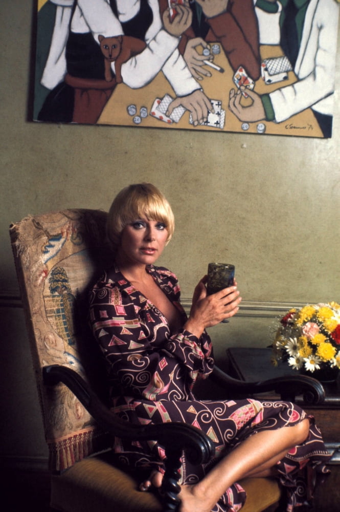 Elke Sommer sitting on a chair holding a glass photo print.