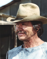 Charles Bronson smiling in a blue shirt and brown hat photo print