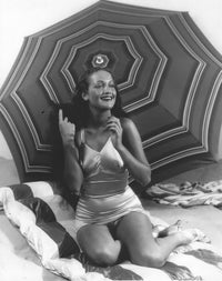 Dorothy Lamour kneeling in front of an umbrella photo print.