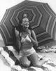 Dorothy Lamour kneeling in front of an umbrella photo print.