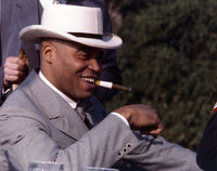 Close-up portrait of James Jones in a grey moire suit and white velvet hat with a cigar.