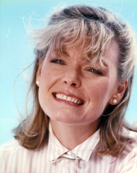 Jane Curtin portrait in beige gingham collar shirt against sky blue background.
